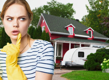 A woman with a questioning look wearing cleaning gloves in front of a red home with a travel trailer out front.