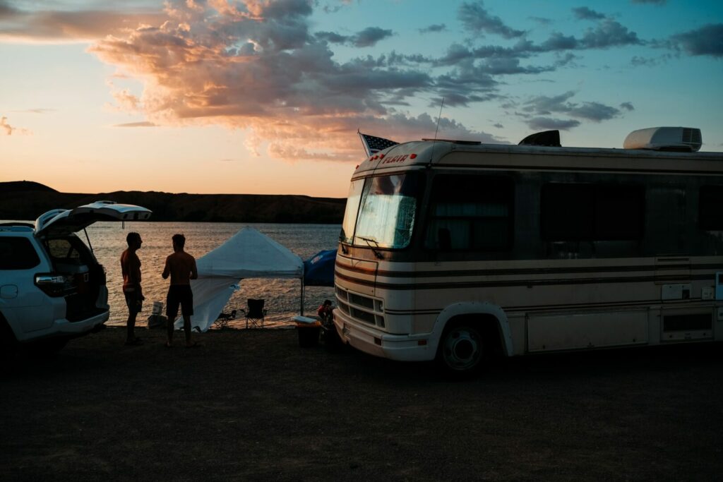 Friends outside enjoying the final moments of a sunset over a lake they are camping next to in a motorhome