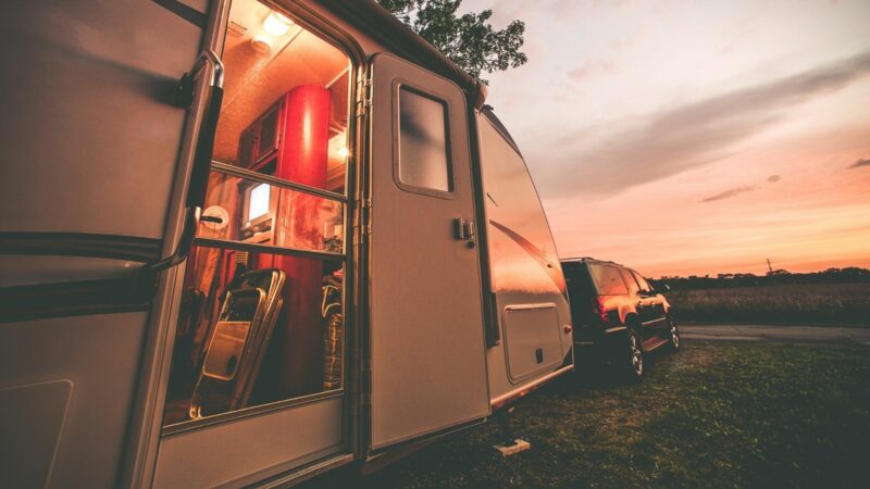 A travel trailer with it's door open at camp during sunset.