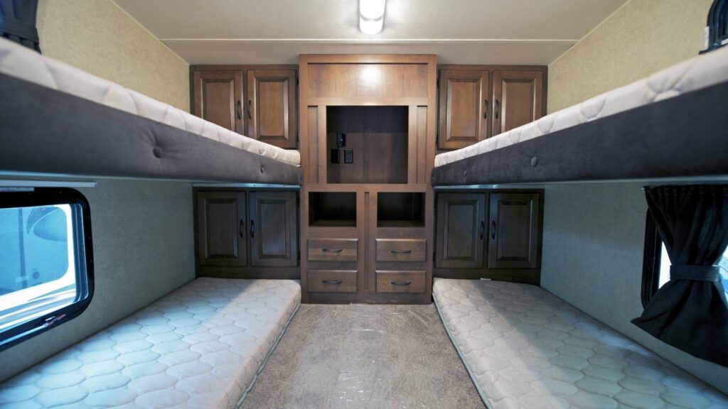 A bunkroom in an RV with four bunk mattresses and storage.