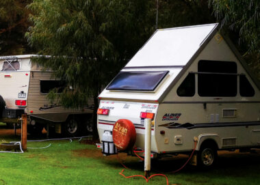 Aliner pop up camper parked in a grassy campsite next to another RV.