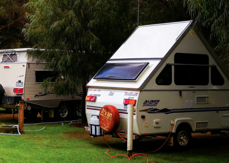 Aliner pop up camper parked in a grassy campsite next to another RV.
