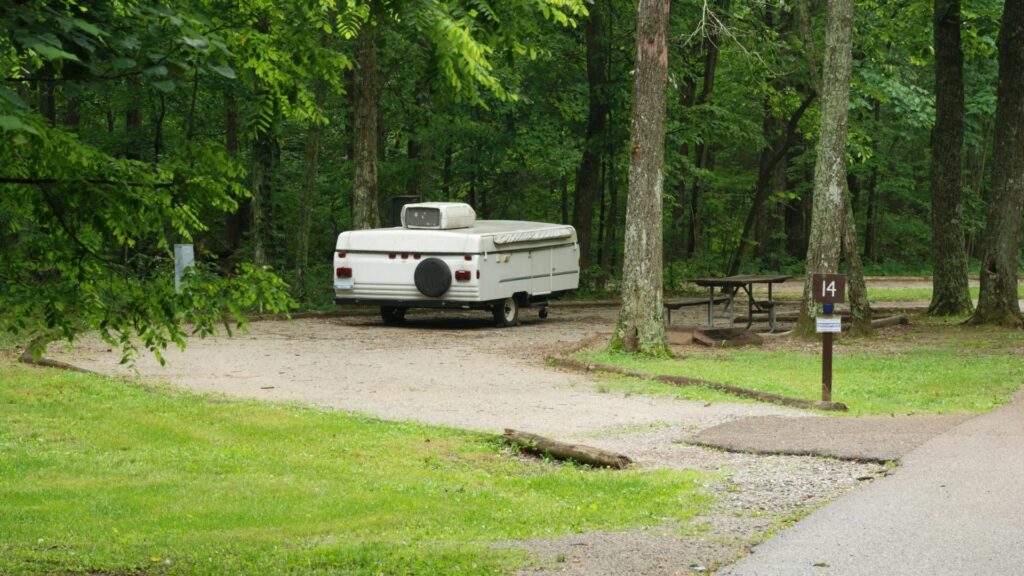 Pop up camper in its closed position at a drive thru campsite in a wooded are.