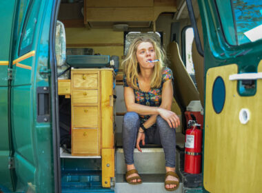An exhausted woman sit lazily in her campervan with her arms crossed and toothbrush hanging out of her mouth.