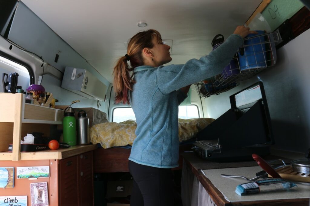 Cramped living in a van, a woman searches for a item she can't find in the kitchen area.