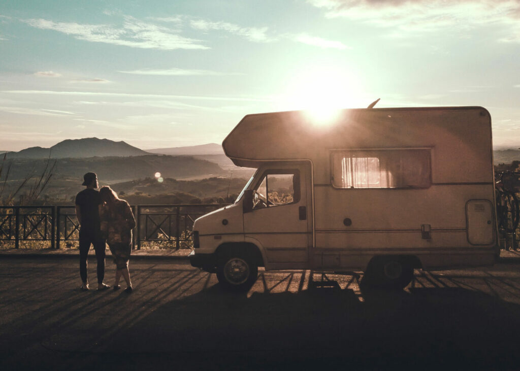 A couple stands outside their RV and watches the sun goes down, leaning on one another