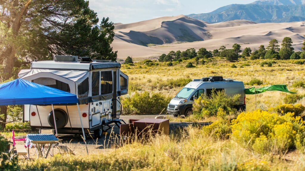 Two RVs, a pop-up camper and a class B, enjoy a remote campsite with the Great Sand Dunes in the distance.