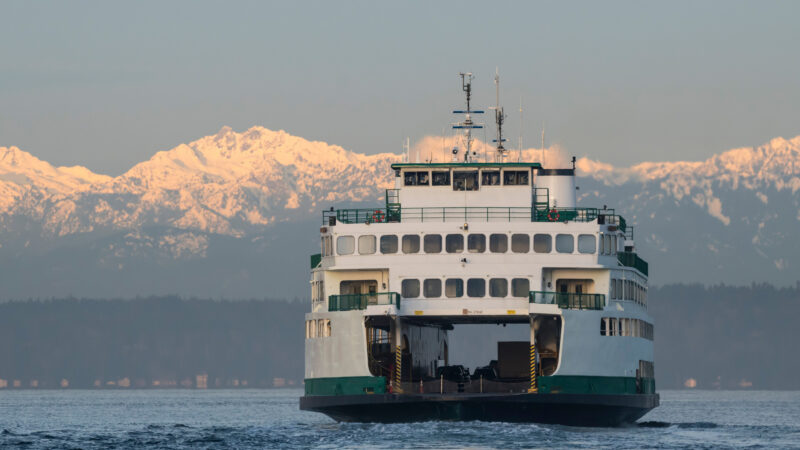 A ferry boat crosses cold pacific northwest waters with snow covered mountains in the background.