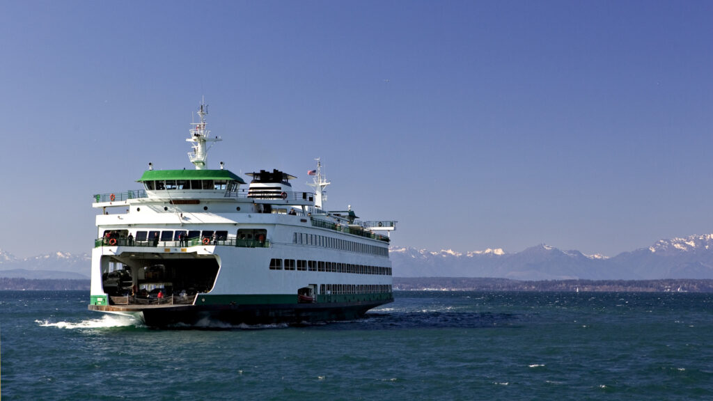 A green and white ferry transports cars, passengers, trucks, and RVs across the Pacific Ocean to Vancouver Island and passes the Olympic Mountains in Washington.