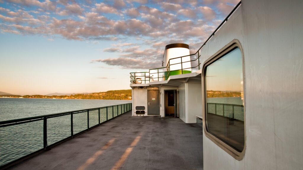 A colorful sky reflects in the windows of the ferry deck as it crosses the waters.