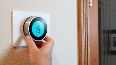 A person's hand turns a smart thermostat to start the air conditioner in their home.