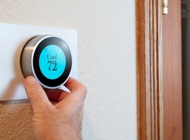 A person's hand turns a smart thermostat to start the air conditioner in their home.