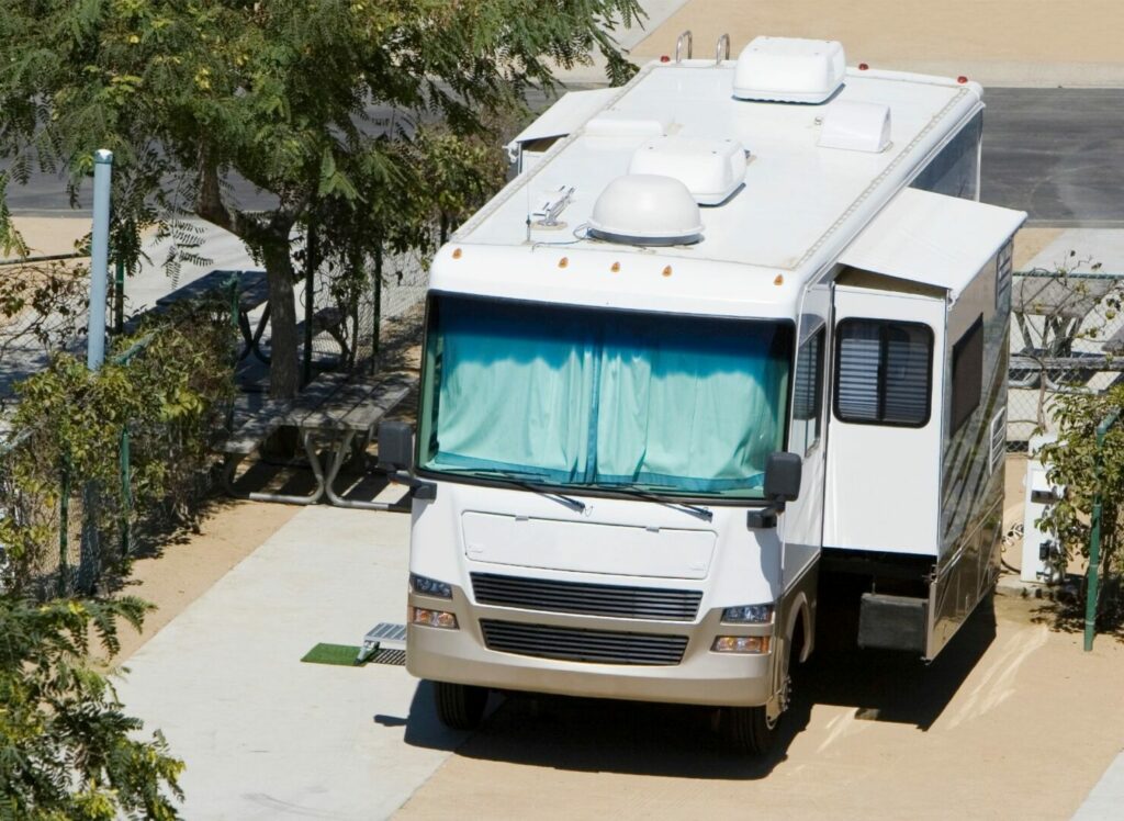 An RV parked at a campground with little shade, all the curtains are drawn to keep out the heat.