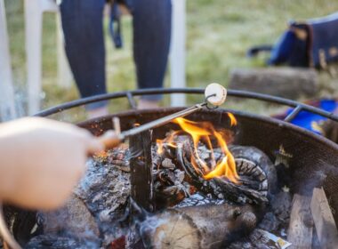 An extendable campfire roasting stick held over a fire with a marshmallow on the end.