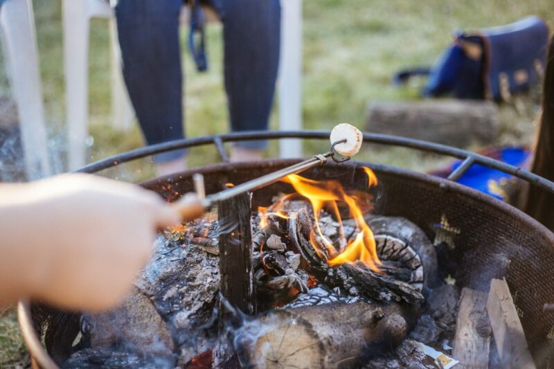 An extendable campfire roasting stick held over a fire with a marshmallow on the end.