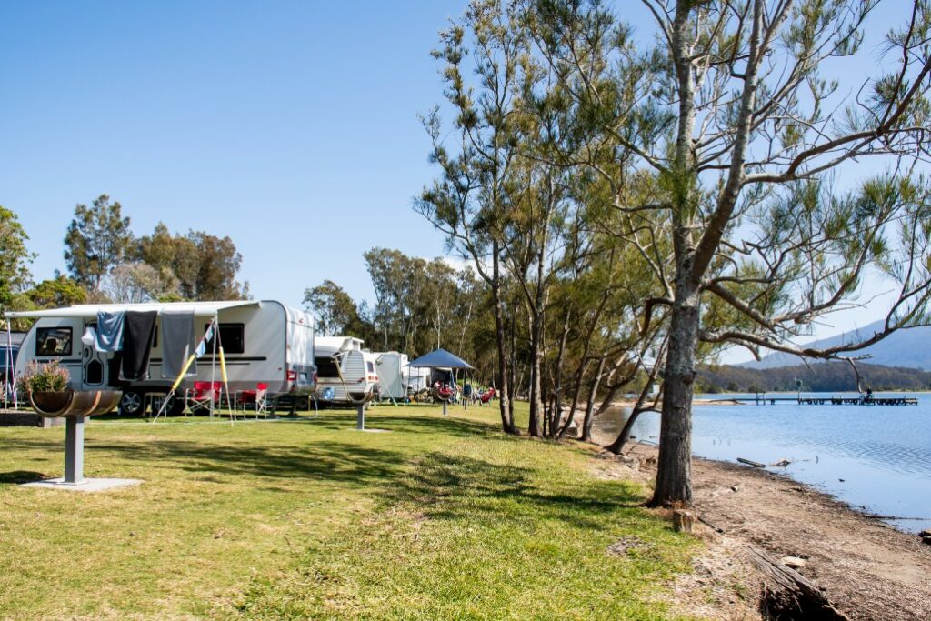 RVs parked along the shoreline of a campgrounds on the water during the day.