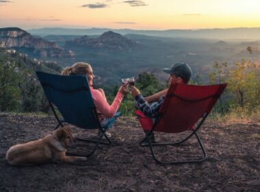 A couple lounges in their reclining camping chairs, drinking wine as the sun sets