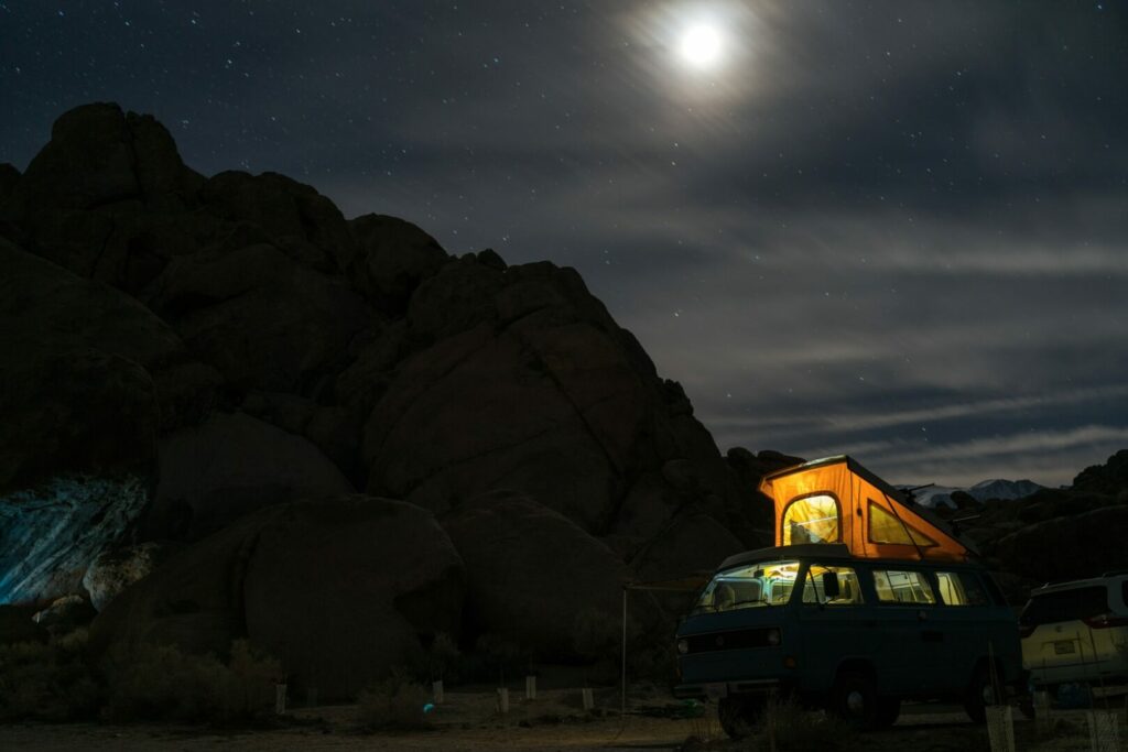 A camper van with pop up top glows with light from the inside on a clear, dark night in the mountains.