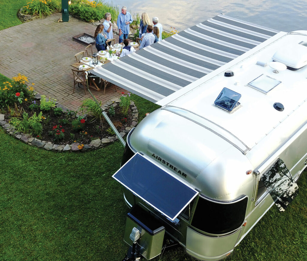 View from above of the Airstream Globetrotter with the striped awning extended and a group enjoying dinner outside.