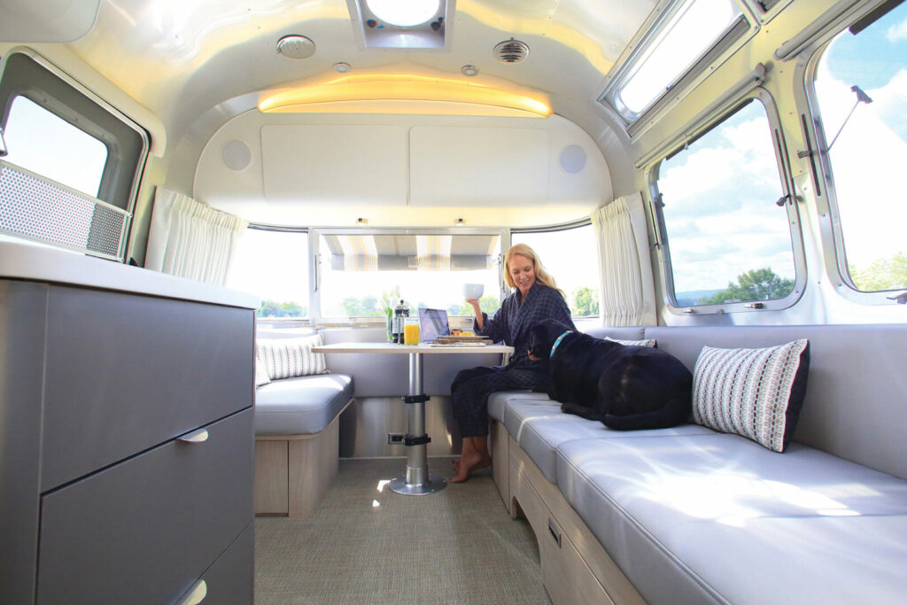 A woman and her dog on the cushioned seats of an Airstream Globetrotter enjoying breakfast at the dining table