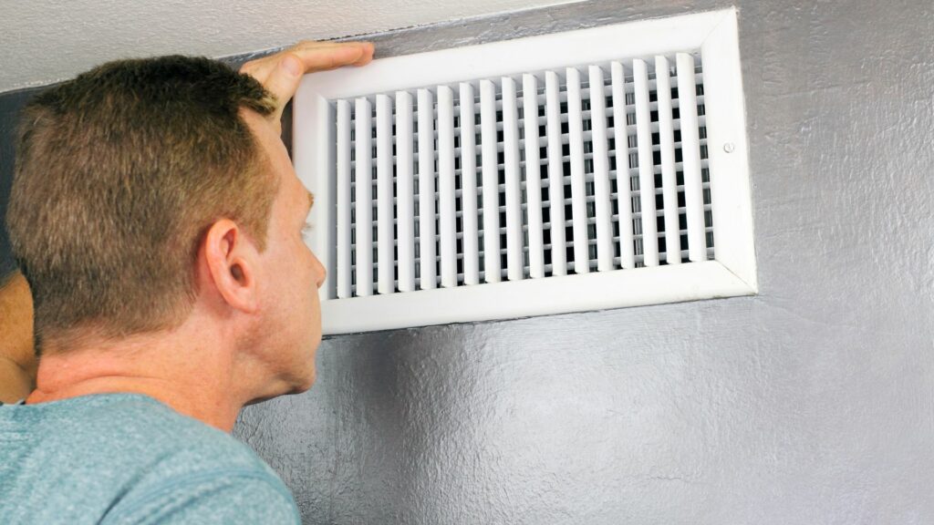 A man inspects the air vent of a heating and cooling system for any blockages.