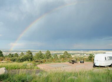 A cute travel trailer parked at a campsite on a hill overlook a rainbow