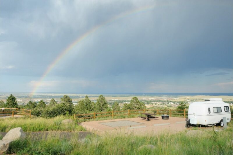 A cute travel trailer parked at a campsite on a hill overlook a rainbow