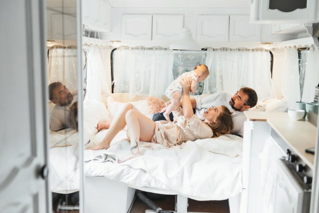 Two parents and their baby play on the bed of a travel trailer.