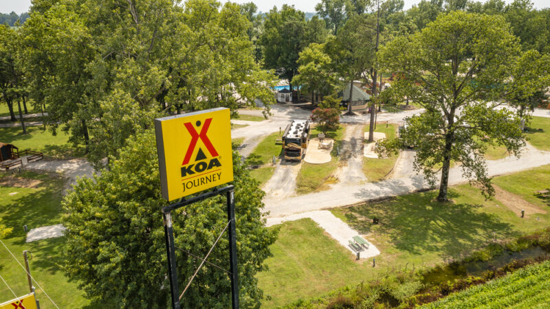 The campground sign at Memphis KOA Journey stands high above the grounds with RVs and a swimming pool
