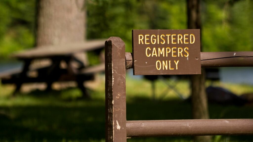 A campground sign telling people you must register with the office to camp.