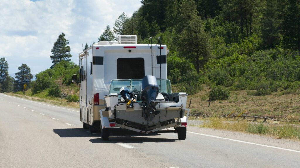 A motorhome pulls a boat on a trailer down a road.