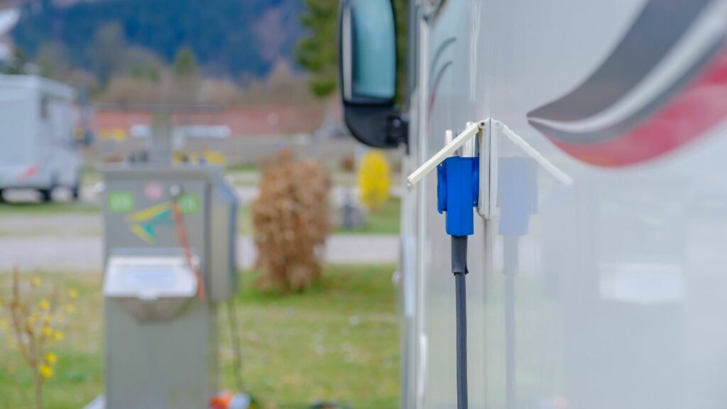 An RV hooked up to a campground electrical box with a power cable.