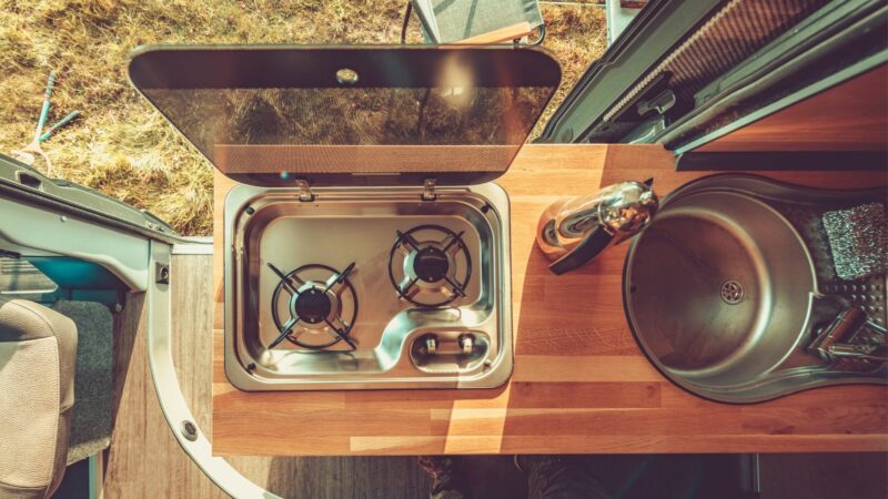 Top down view of an RV stove top with the cover lifted open.