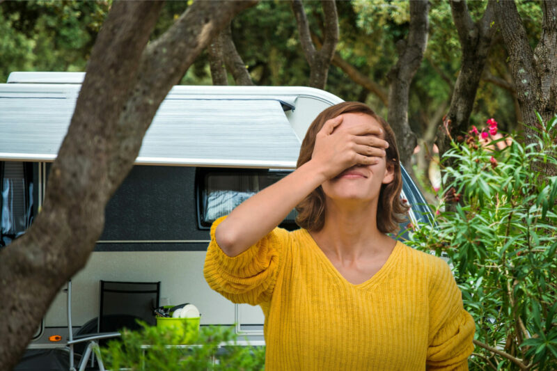 A woman face palms out of frustration outside an RV parked in a campground