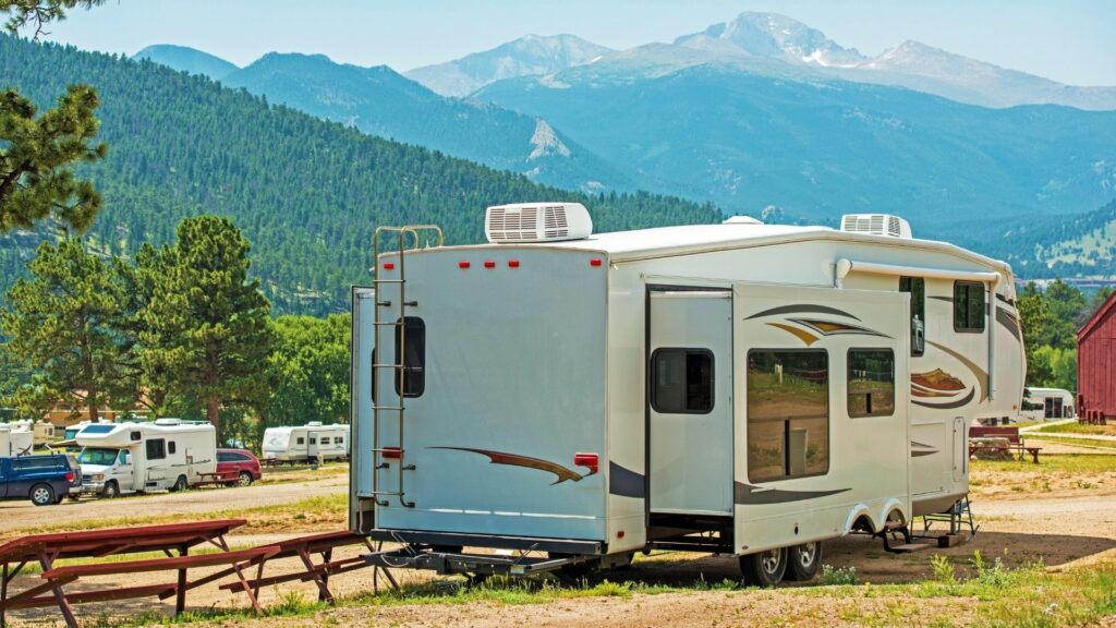 An RV is parked level at a beautiful campsite on a hill with mountains in the distance.