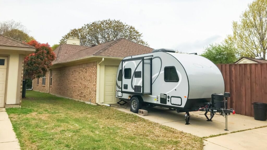 A travel trailer sits in the driveway of a home because it is too large to fit into the garage.