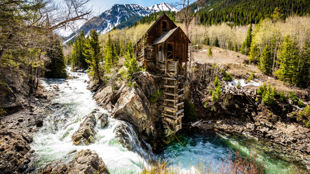 A cabin on the edge of a cliff above a river with snowy mountains in the back of beautiful White River National Forest.