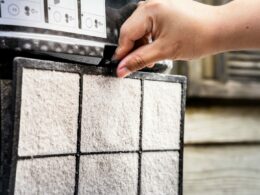 A hand removes a dirty air filter to clean and replace