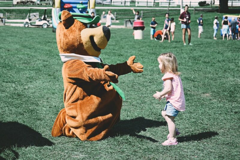 A little girl runs up to a Yogi Bear mascot to give him a hug at a Jellystone RV Park.