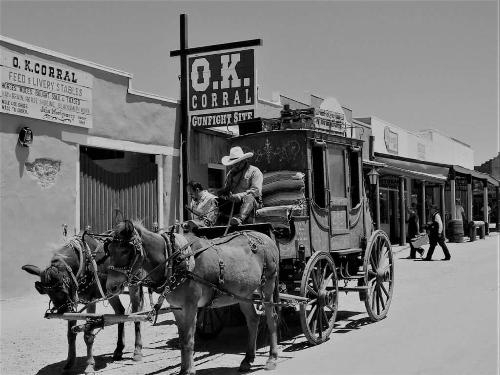 A cowboy drives a stagecoach pulled by mules and carrying passengers, past the famous OK Corral tourist attraction
