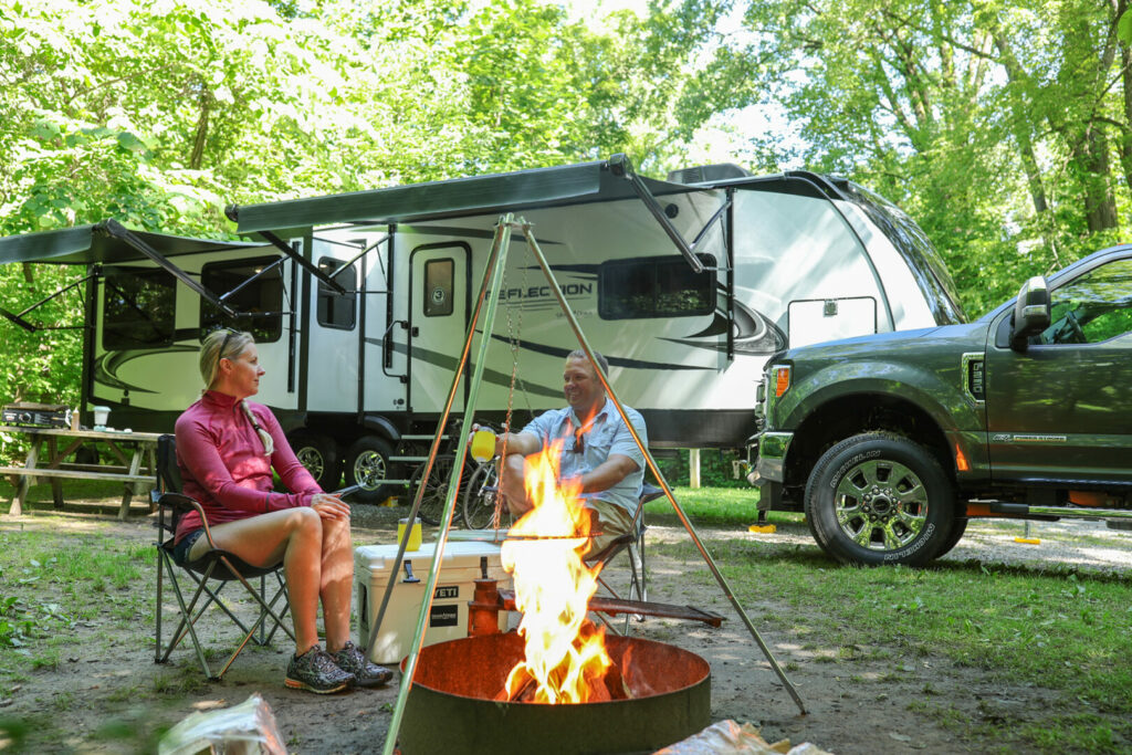 A couple sits outside their Grand Design Reflection RV enjoying a campfire.