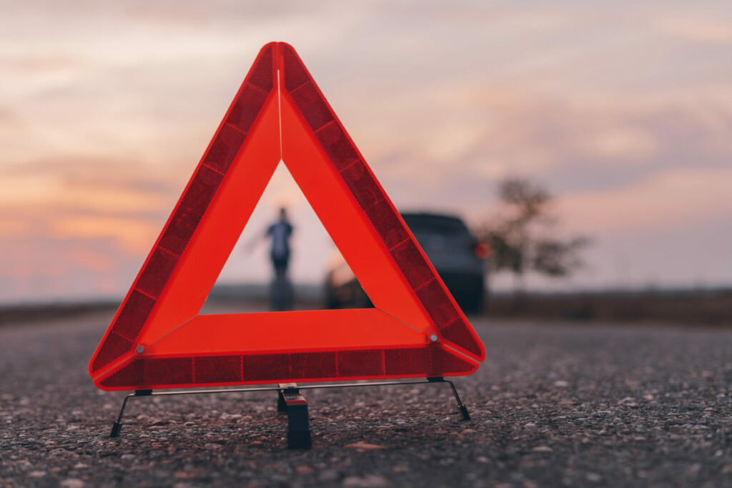 Warning triangle sign on the road, woman in blur background calling for roadside assistance by the broken car, selective focus