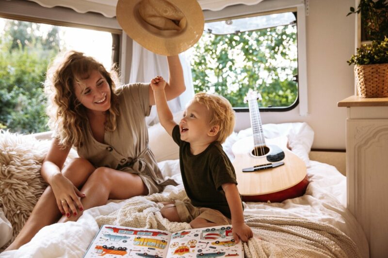Carefree young mother playing with her young son sitting on the bed in an RV travel trailer.