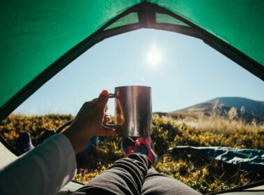 The morning sun beams through the tent door and a camper holds up his coffee mug as he relaxes.