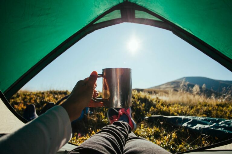 The morning sun beams through the tent door and a camper holds up his coffee mug as he relaxes.