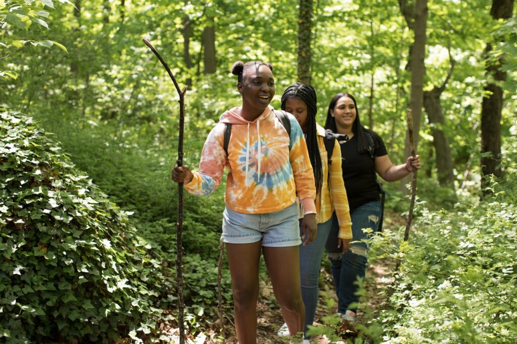 Three young woman hike through a forest trail using sticks for balance.