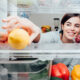 A woman reaches into a fridge for a healthy yellow lemon.