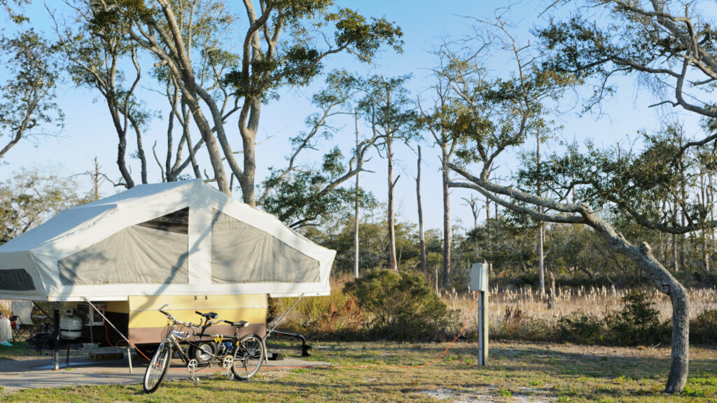 A pop up camper is set up in a campground with a bike parked in front. 