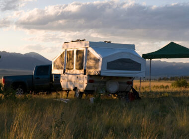 A pop up camper has made a nice campsite out in an open field with some trees and mountains nearby.