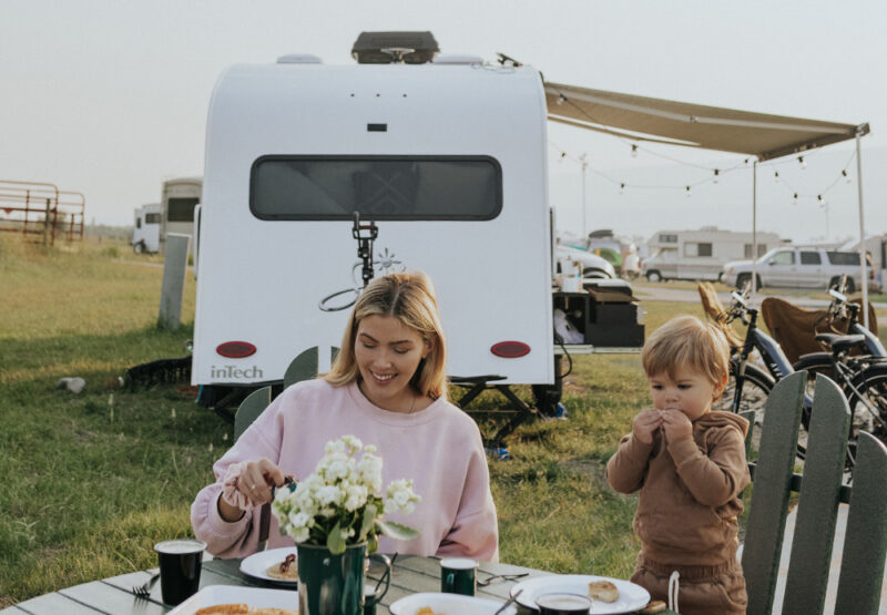 A happy young family sits at the campground with their InTech trailer camped up behind them.
